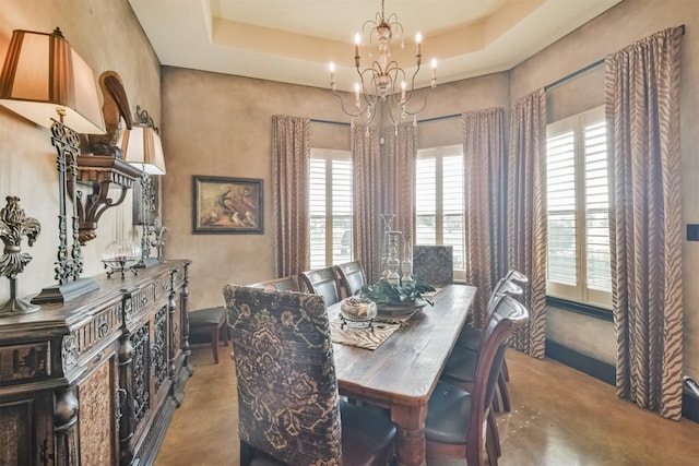 dining area with an inviting chandelier, a tray ceiling, and concrete flooring