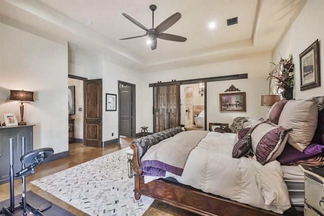 bedroom featuring a barn door, visible vents, a raised ceiling, a ceiling fan, and baseboards