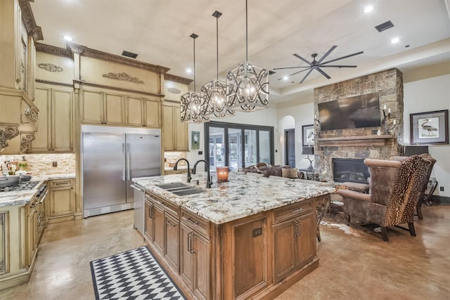 kitchen featuring a sink, hanging light fixtures, appliances with stainless steel finishes, light stone countertops, and a center island with sink