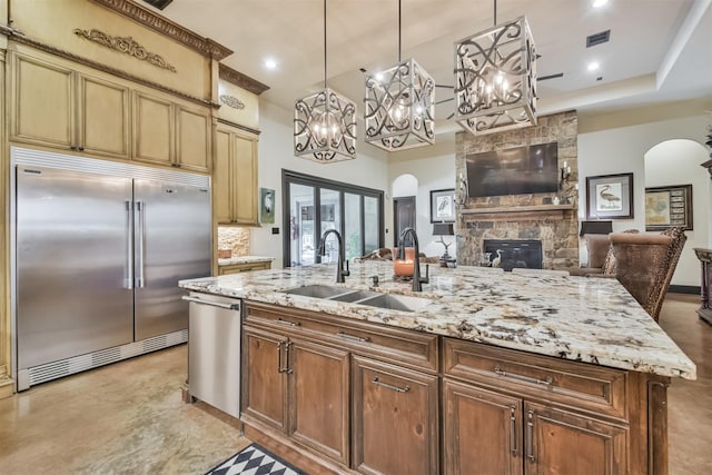 kitchen featuring an island with sink, arched walkways, stainless steel appliances, and a sink