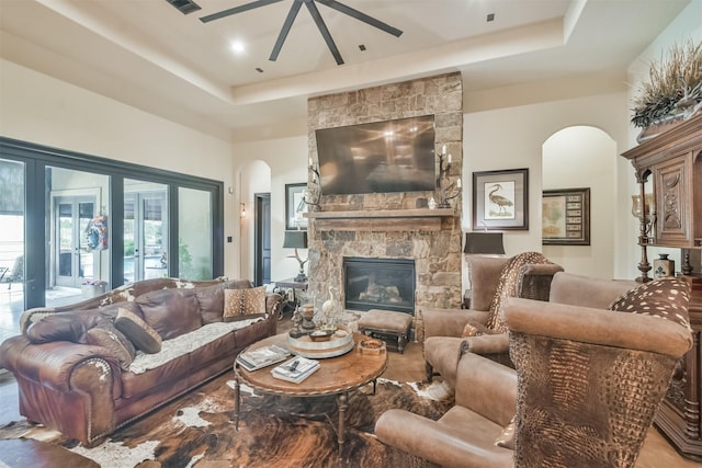 living room with arched walkways, a fireplace, a raised ceiling, visible vents, and ceiling fan