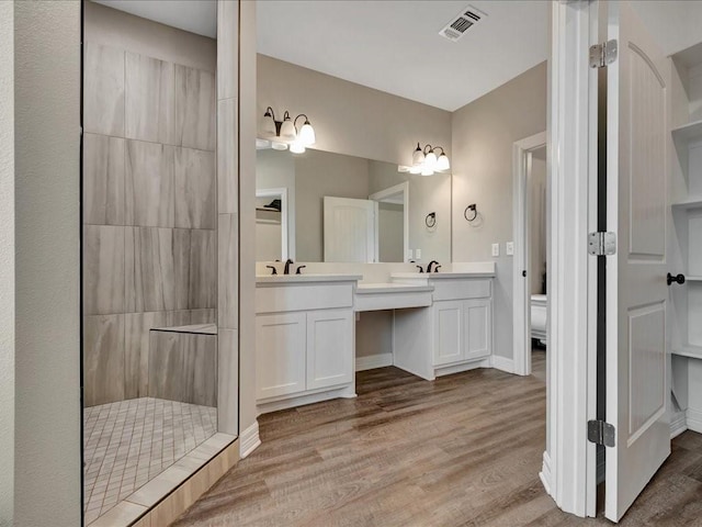 bathroom with vanity, toilet, hardwood / wood-style floors, and a tile shower