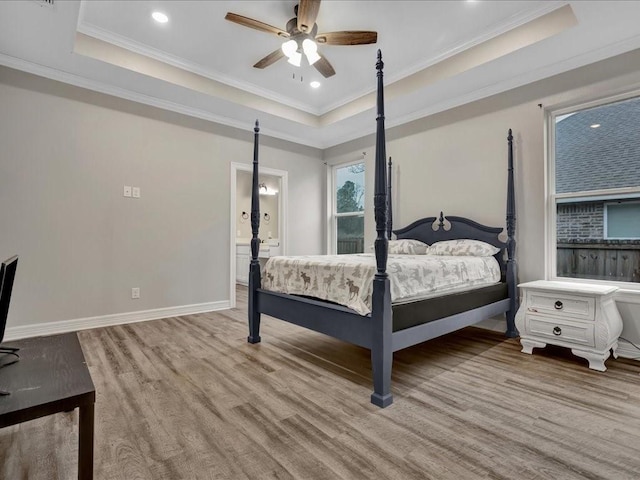 bedroom with crown molding, ensuite bath, ceiling fan, a tray ceiling, and light hardwood / wood-style floors