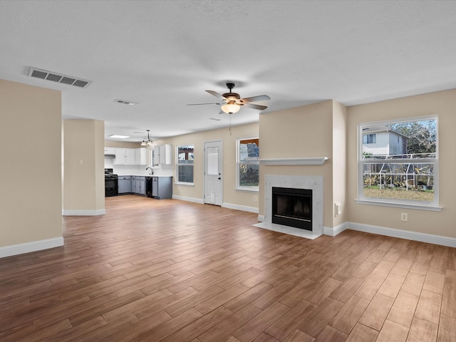 unfurnished living room with ceiling fan, a premium fireplace, and light hardwood / wood-style floors