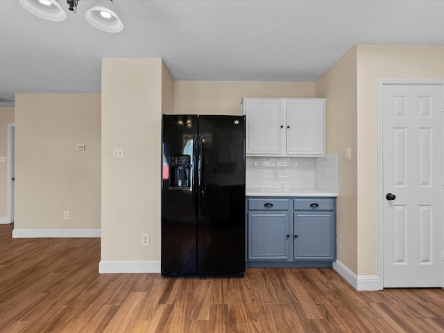 kitchen featuring tasteful backsplash, white cabinetry, black fridge, and wood-type flooring