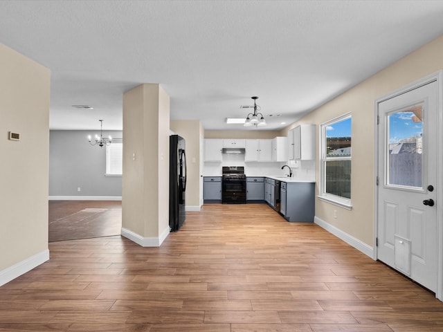 kitchen with sink, range with gas cooktop, decorative light fixtures, black refrigerator, and a notable chandelier