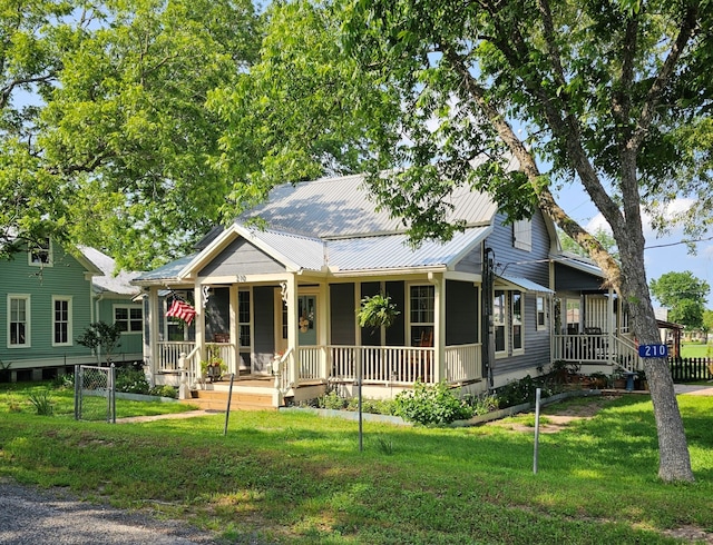 view of front of home featuring covered porch, metal roof, fence, and a front lawn