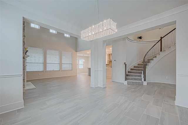 unfurnished living room featuring a towering ceiling, a notable chandelier, and light hardwood / wood-style floors