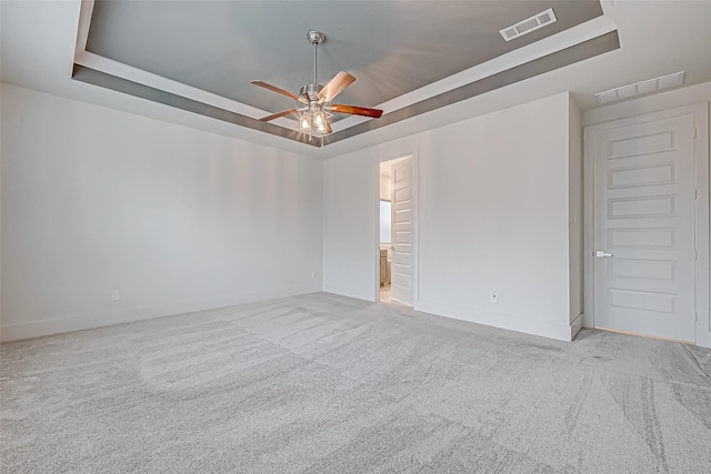 empty room with a raised ceiling, light colored carpet, and ceiling fan