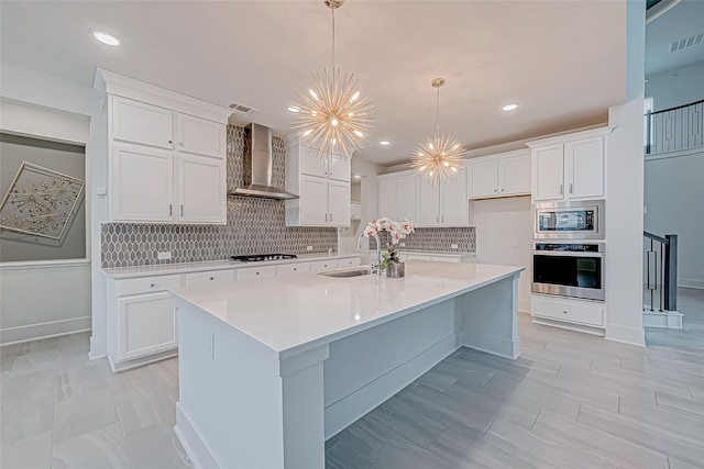 kitchen featuring sink, an inviting chandelier, appliances with stainless steel finishes, wall chimney range hood, and white cabinets