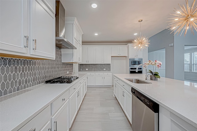 kitchen featuring appliances with stainless steel finishes, sink, white cabinets, wall chimney range hood, and an inviting chandelier