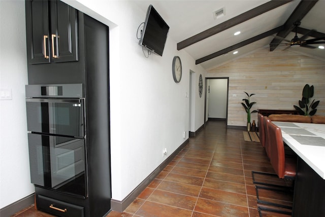 kitchen with lofted ceiling with beams, black double oven, dark tile patterned floors, and ceiling fan