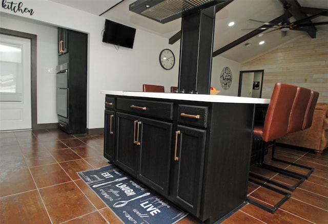 interior space featuring a kitchen island, lofted ceiling with beams, a kitchen breakfast bar, double wall oven, and ceiling fan