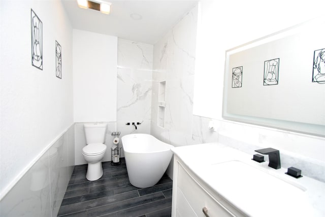 bathroom with tile walls, hardwood / wood-style floors, vanity, a bath, and toilet