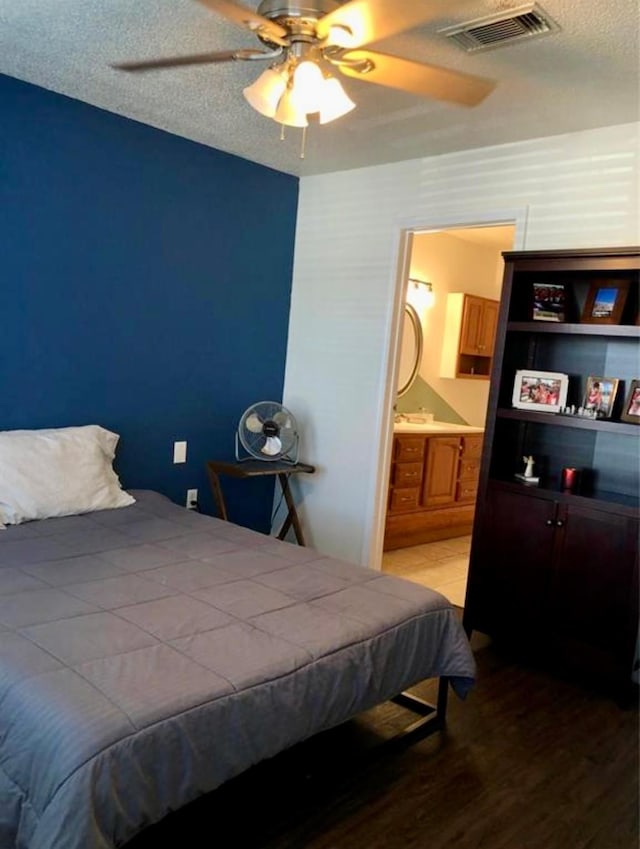 bedroom featuring ceiling fan, hardwood / wood-style floors, a textured ceiling, and ensuite bath