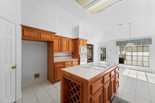 kitchen with tile countertops, hanging light fixtures, light tile patterned floors, a kitchen island, and white appliances