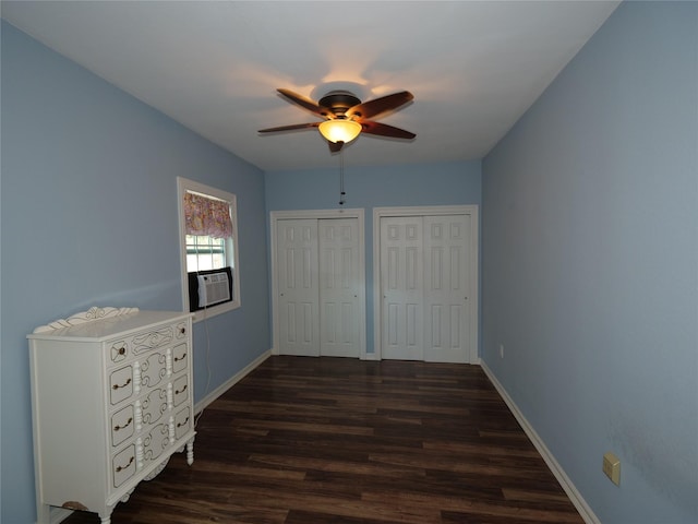 unfurnished bedroom featuring dark wood-type flooring, two closets, ceiling fan, and cooling unit