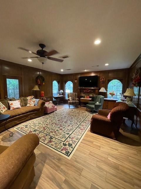 living room featuring wood walls, ceiling fan, and light hardwood / wood-style flooring