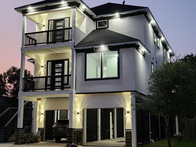 view of front of property featuring roof with shingles, stucco siding, concrete driveway, a balcony, and stairs