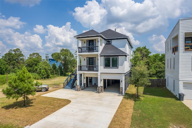 raised beach house with a balcony, stairs, concrete driveway, roof with shingles, and a carport