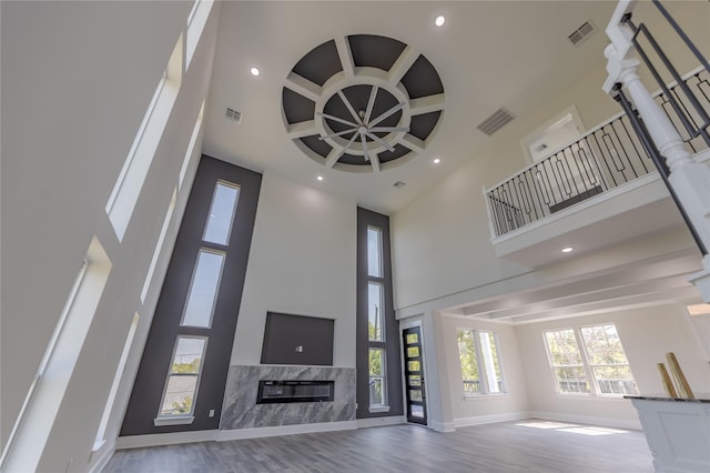 unfurnished living room featuring light wood finished floors, a high ceiling, a high end fireplace, and visible vents