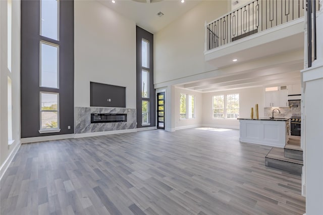 unfurnished living room with light wood-type flooring, a high end fireplace, a sink, and baseboards