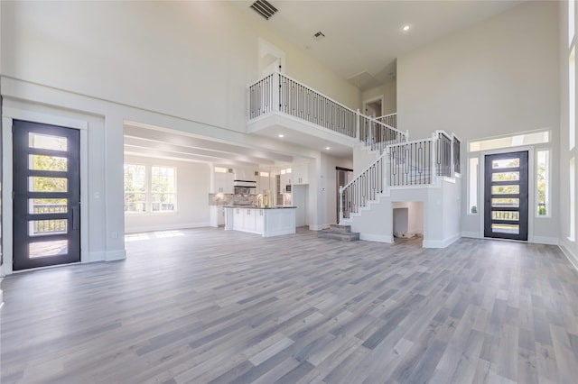 unfurnished living room with baseboards, visible vents, wood finished floors, a high ceiling, and stairs