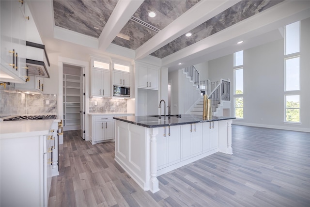 kitchen featuring a kitchen island with sink, stainless steel microwave, a kitchen bar, and white cabinetry