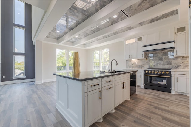 kitchen with a center island with sink, glass insert cabinets, white cabinetry, a sink, and black appliances