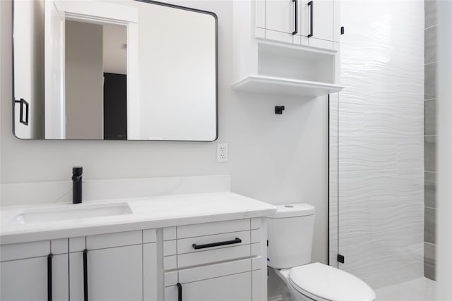 bathroom with toilet, tiled shower, and vanity