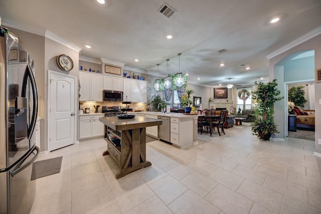 kitchen with pendant lighting, appliances with stainless steel finishes, white cabinetry, a kitchen island, and decorative backsplash