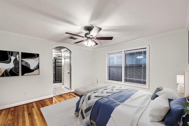 bedroom with connected bathroom, hardwood / wood-style flooring, ornamental molding, and ceiling fan