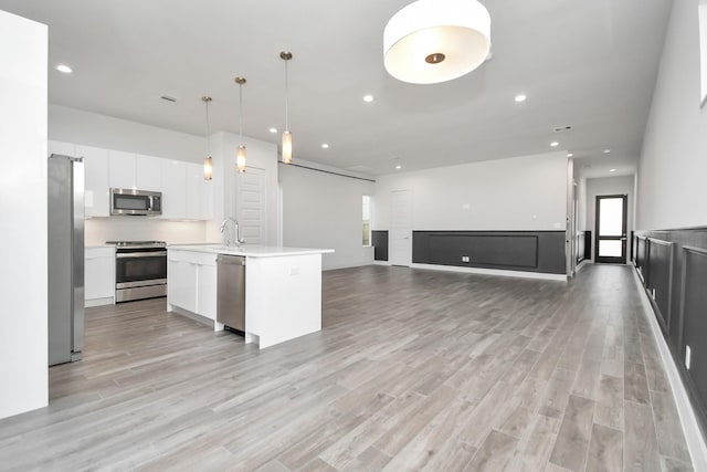 kitchen with pendant lighting, white cabinetry, a kitchen island with sink, stainless steel appliances, and light hardwood / wood-style floors