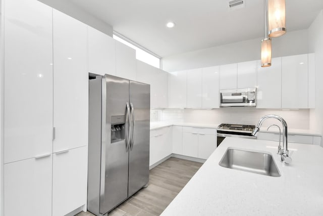 kitchen with stainless steel appliances, white cabinetry, hanging light fixtures, and sink