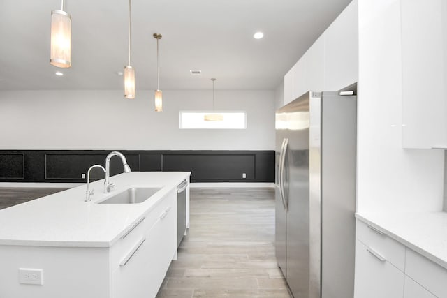 kitchen featuring sink, white cabinetry, stainless steel appliances, decorative light fixtures, and light wood-type flooring