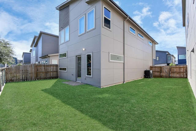 rear view of house featuring central AC unit and a lawn