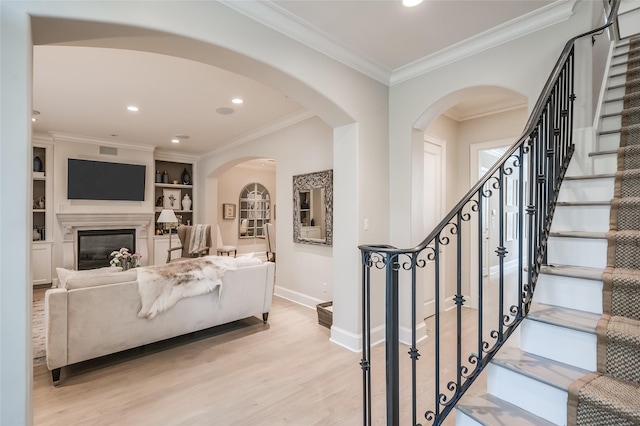 living room with built in features, ornamental molding, and light wood-type flooring