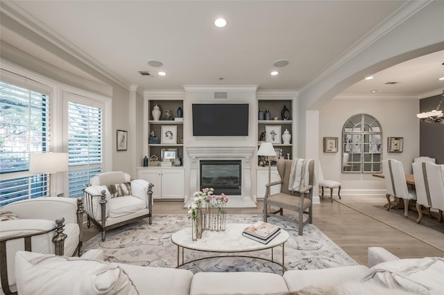 living room with crown molding, light hardwood / wood-style flooring, a premium fireplace, built in shelves, and a chandelier