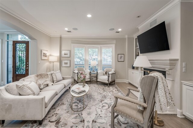 living room with crown molding, built in features, a high end fireplace, and light hardwood / wood-style flooring