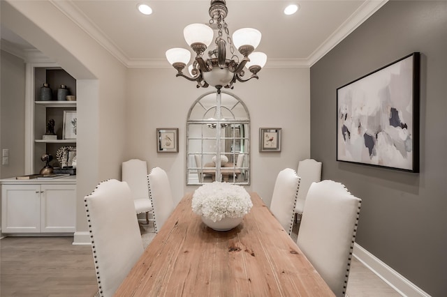 dining room with built in shelves, ornamental molding, a chandelier, and light hardwood / wood-style floors