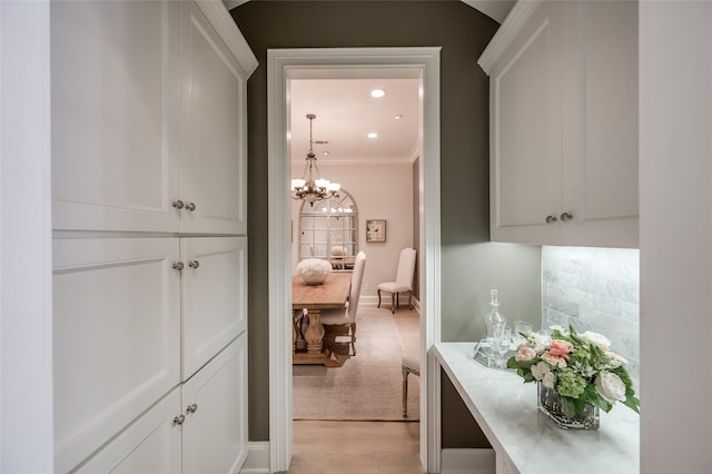 hallway with light hardwood / wood-style flooring, ornamental molding, and a chandelier