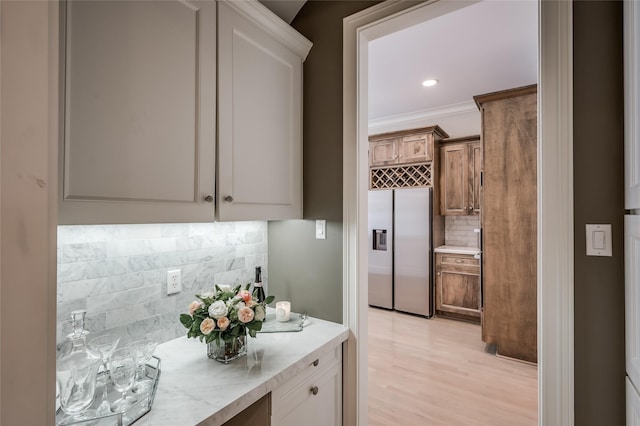 kitchen with tasteful backsplash, ornamental molding, stainless steel built in fridge, and light wood-type flooring