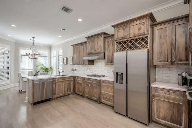 kitchen with sink, crown molding, decorative light fixtures, stainless steel appliances, and light hardwood / wood-style floors