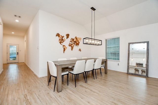 dining area with an inviting chandelier, light hardwood / wood-style flooring, and lofted ceiling