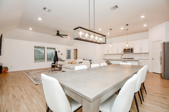 dining area with ceiling fan, lofted ceiling, sink, and light wood-type flooring