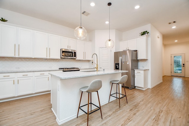 kitchen with sink, appliances with stainless steel finishes, hanging light fixtures, an island with sink, and white cabinets