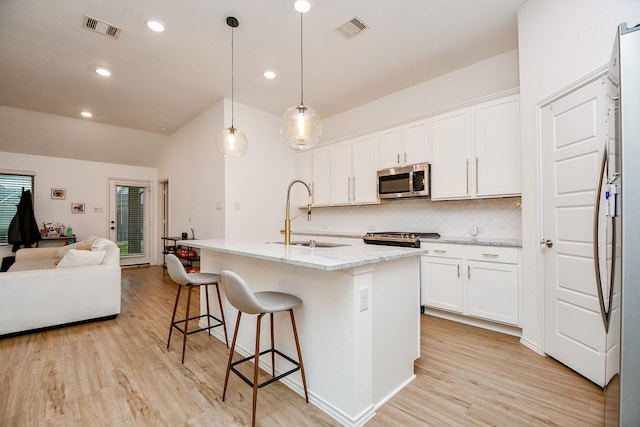 kitchen featuring sink, white cabinetry, hanging light fixtures, stainless steel appliances, and a center island with sink