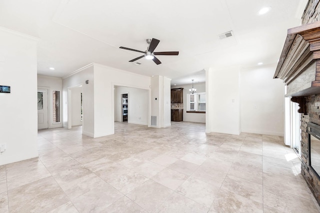 unfurnished living room with crown molding, a stone fireplace, and ceiling fan with notable chandelier