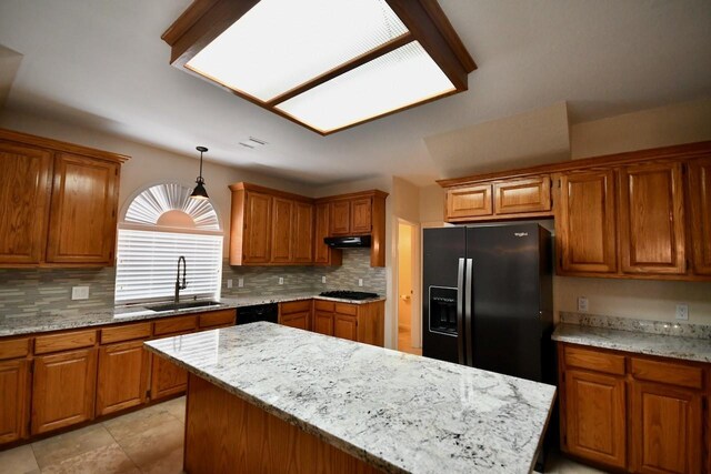 kitchen featuring sink, tasteful backsplash, light stone counters, hanging light fixtures, and black appliances