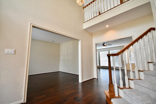 entryway with a towering ceiling, dark wood-type flooring, and ceiling fan